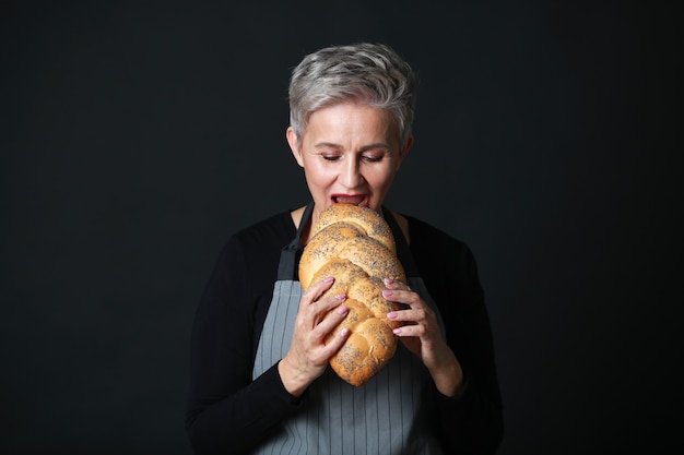 schöne alte Frau in Schürze beißt Brot