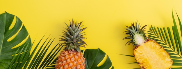 Schöne Ananas auf tropischen Palmen-Monstera-Blättern isoliert auf hellem pastellgelbem Hintergrund Draufsicht flach lag oben über Sommerfrucht
