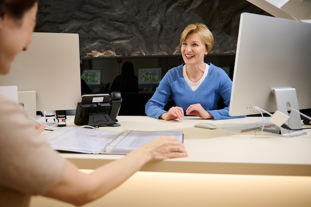 Foto schöne angenehme kaukasische reiseagentin, die mit ihrem kunden spricht und katalog mit touren oder verbraucherdienstleistungen zeigt, während sie in einem modernen büro sitzt