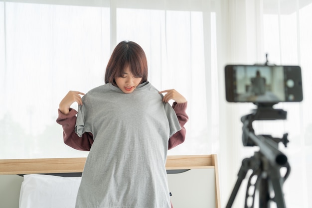 Schöne asiatische Bloggerin, die Kleidung vor der Kamera zeigt, um Vlog-Video-Live-Streaming in ihrem Shop aufzunehmen - Online-Influencer auf Social-Media-Konzept