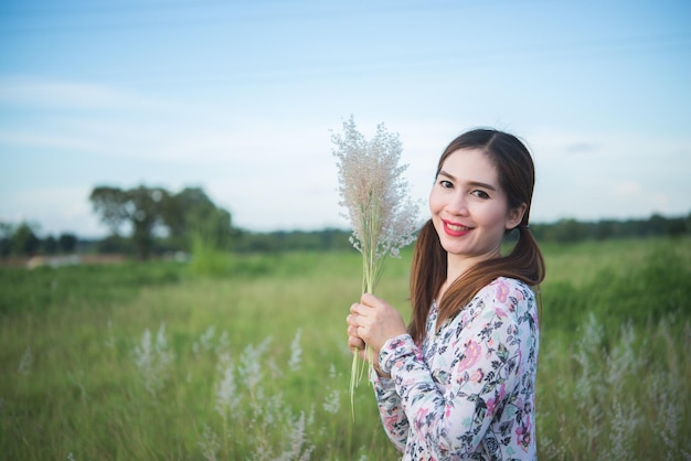 Schöne asiatische Frau, die am Abend Grasblume auf dem Feld hältThailand-Leute