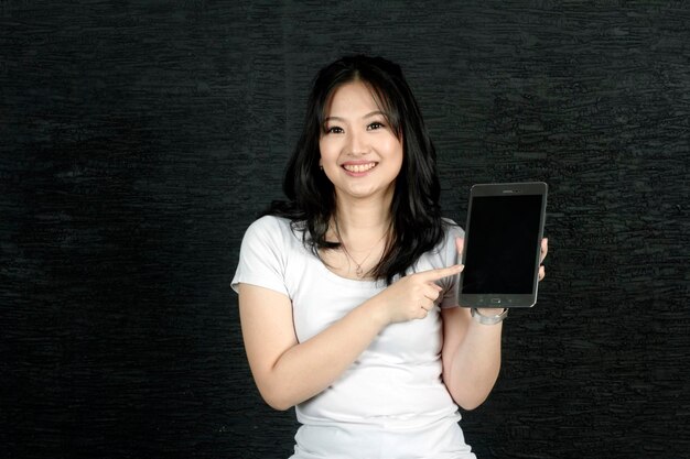 Schöne asiatische Frau, die auf das Tabletlächeln zeigt