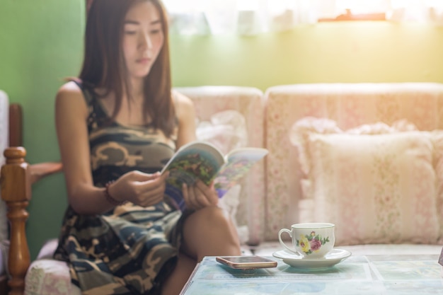 Schöne asiatische Frau, die auf dem Stuhl zu Hause sich entspannt mit Kaffee sitzt