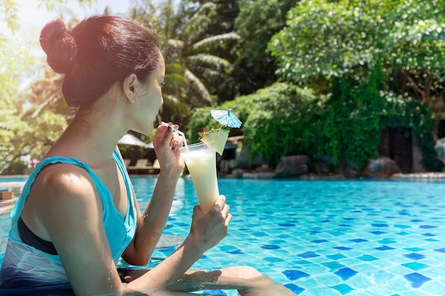 Schöne asiatische Frau, die Cocktail im Swimmingpool isst