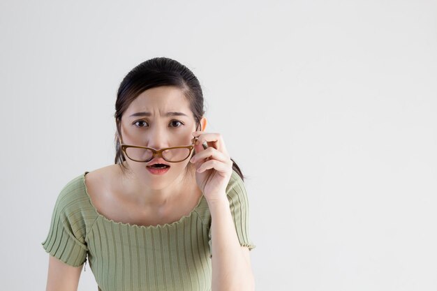 Schöne asiatische Frau, die ein grünes T-Shirt trägt und eine Brille trägt, hat Sehprobleme und kann nicht lesen und hat ein schlechtes Sehvermögen mit einem besorgten Gesicht.