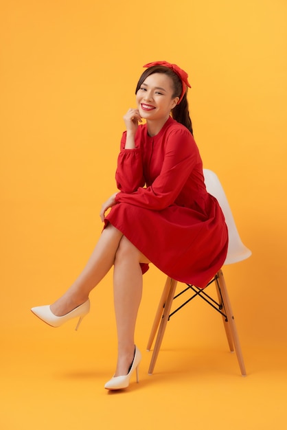Schöne asiatische Frau, die ein rotes Kleid trägt und über einem orange Hintergrund steht