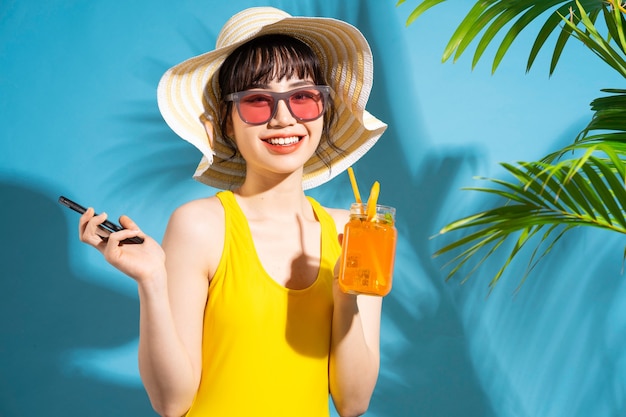 Schöne asiatische Frau, die gelben Overall auf Blau trägt und Saft trinkt