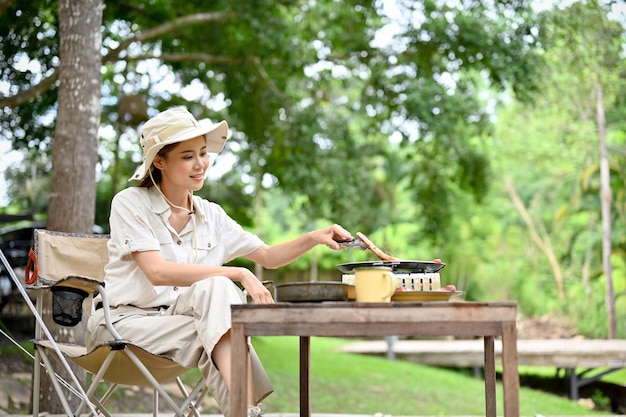 Schöne asiatische frau, die grill auf dem grünen campingplatz vorbereitet outdoor-aktivitätskonzept