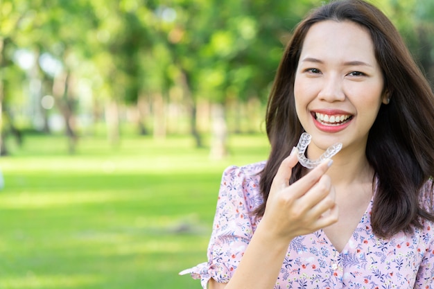 schöne asiatische Frau, die mit der Hand hält zahnmedizinischen Ausrichtungshalter Naturpark am im Freien lächelt