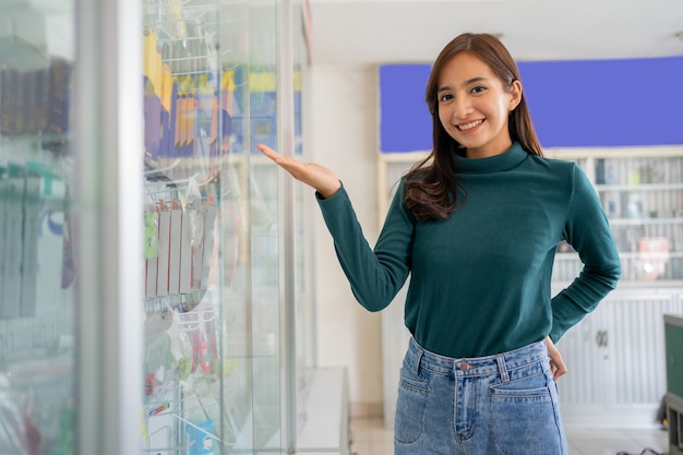 Schöne asiatische frau, die mit handgeste lächelt, die etwas in der nähe von handyzubeh...