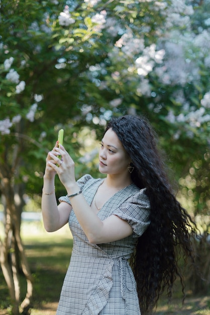 Schöne asiatische Frau, die mit ihrem Smartphone vor den blühenden Bäumen fotografiert