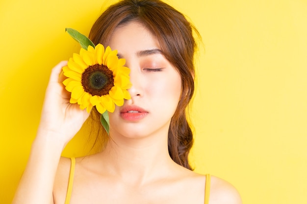 Schöne asiatische Frau, die mit Sonnenblume auf Gelb hält und aufwirft