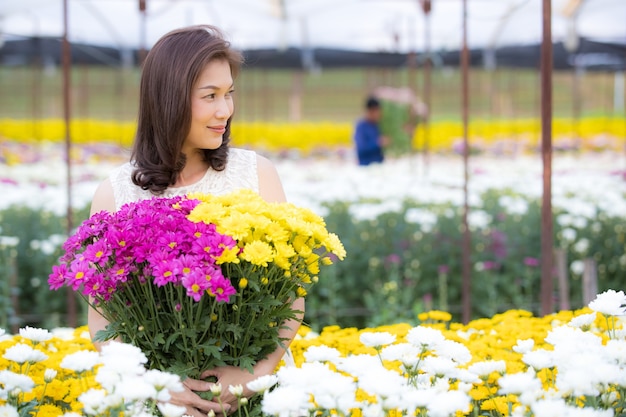 Schöne asiatische Frau, die mit Stolz gelbe Blumen in den Händen hält, Blumengartenbesitzer zufrieden mit Blumen von guter Qualität zum Verkauf.