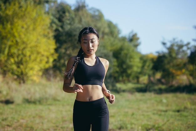 Schöne asiatische Frau, die morgens im Park läuft, eine Frau in einem dunklen Sportanzug