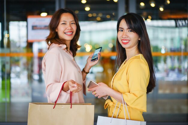 Foto schöne asiatische frau, die tasche und smartphone beim endeinkauf im einkaufszentrum hält