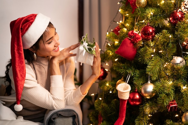 Schöne asiatische Frau, die Weihnachtsverzierung für das Verzieren des Weihnachtsbaumes hält