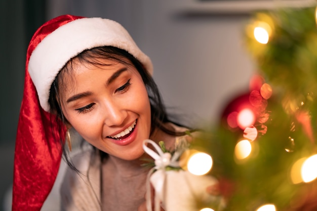 Schöne asiatische Frau, die Weihnachtsverzierung für verzieren auf Weihnachtsbaum hält.