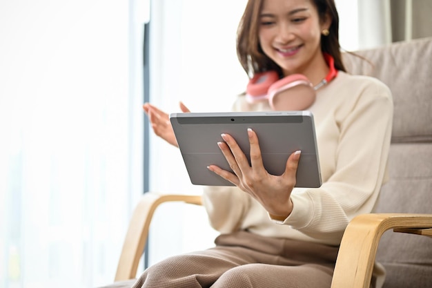 Schöne asiatische Frau entspannt sich im Wohnzimmer mit einem digitalen Tablet-Touchpad