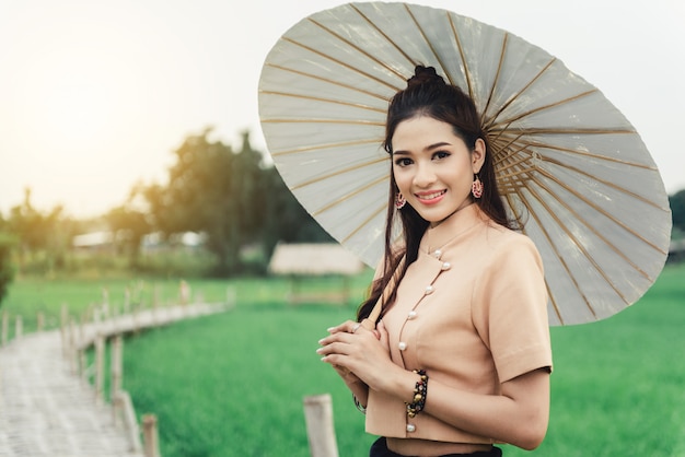 Schöne asiatische Frau im lokalen Kleid, das Papierregenschirmstellung hält