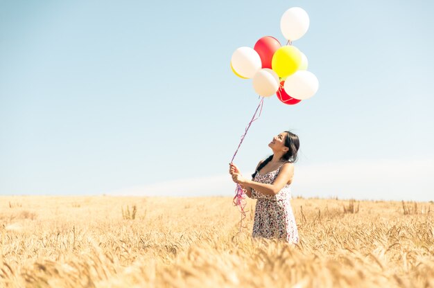 Schöne asiatische Frau in einem Weizenfeld mit Luftballons