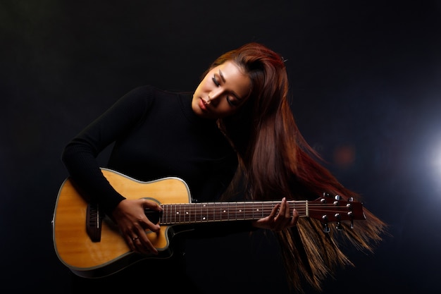 Schöne asiatische Frau lange braune schwarze Haare spielen Gitarre und singen ein Lied auf der Bühne mit Licht Rauch