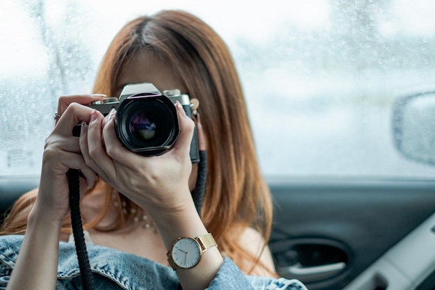 Schöne asiatische Frau mit Kamera im Auto gegen Regentropfenhintergrund