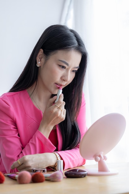 Schöne asiatische Frau mit weißer Haut, die einen Spiegel aufträgt, der rosa Lippenstift aufträgt