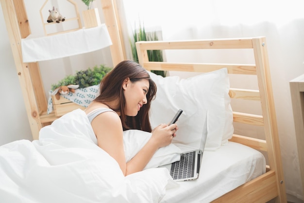 Schöne asiatische Frau nutzt Laptop und Smartphone im Schlafzimmer zum Online-Shopping. Asiatisches Frauen-Lifestyle-Konzept