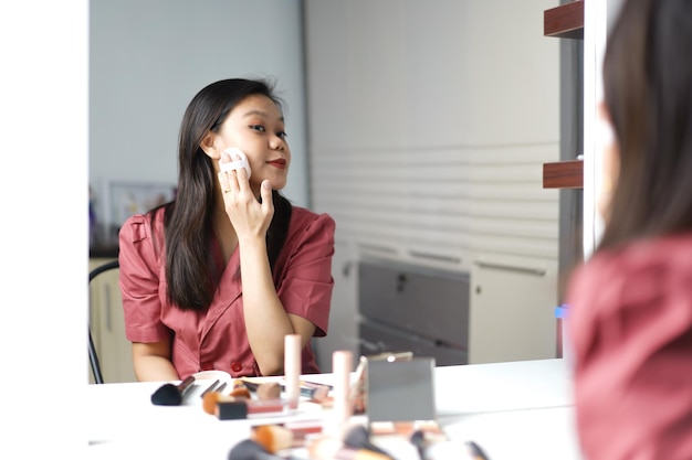 Schöne asiatische Frau schminkt sich vor einem Schminktischspiegel