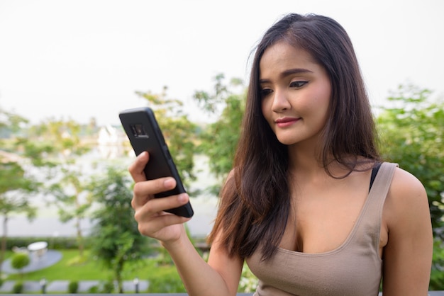 Schöne asiatische Frau SMS mit Handy im Freien