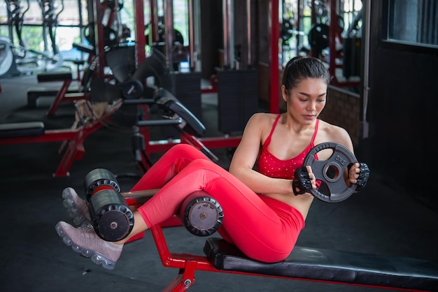 Schöne asiatische Frau spielt Fitness im FitnessstudioThailändisches Mädchen hat einen schlanken KörperZeit für BewegungMenschen lieben Heide Heben Sie den Teller auf der Bank hoch