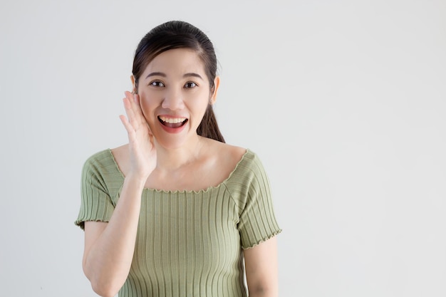 Schöne asiatische Frau trägt grünes T-Shirt und erzählt oder flüstert geheime Nachrichten und Informationen.