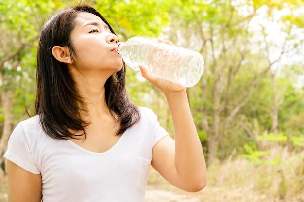 Schöne asiatische Frau trinkt frisches Wasser in einer Flasche im Freien mit Naturhintergrund