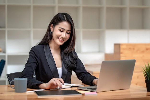 Schöne asiatische Geschäftsfrau arbeitet mit einem Tablet und einem Laptop mit Dokumenten im Büro.