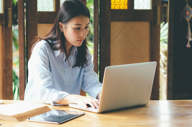 Schöne asiatische Geschäftsfrau, die mit Laptop, Handy und Tablette arbeitet.