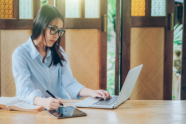 Schöne asiatische Geschäftsfrau, die mit Laptop, Telefon und Tablette arbeitet