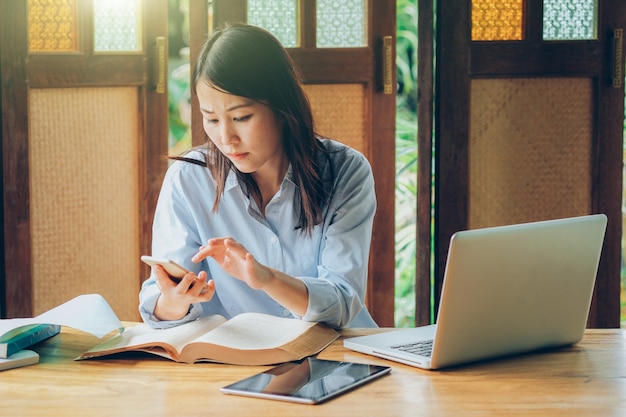 Schöne asiatische Geschäftsfrau, die mit Laptop, Telefon und Tablette im Weinleseton arbeitet