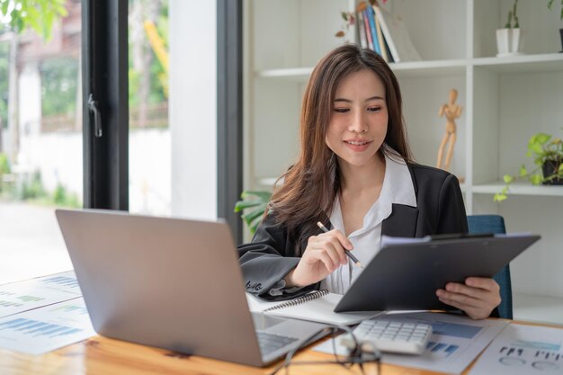 Schöne asiatische Geschäftsfrauen überprüfen Dokumente und benutzen Notizbücher und lächeln glücklich über ihre Arbeit