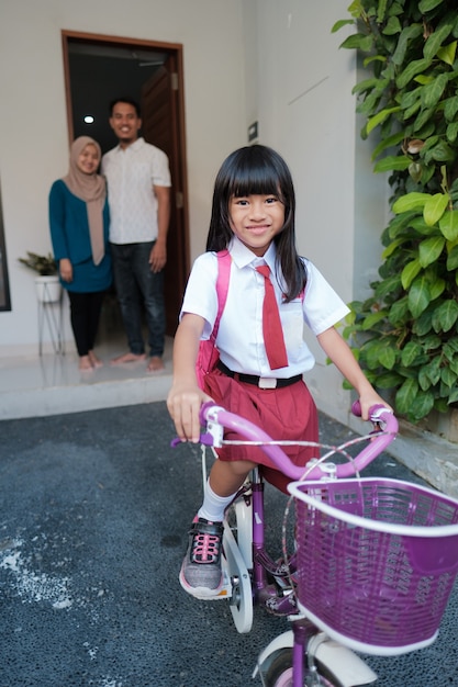 Schöne asiatische Grundschülerin, die morgens mit dem Fahrrad zur Schule geht