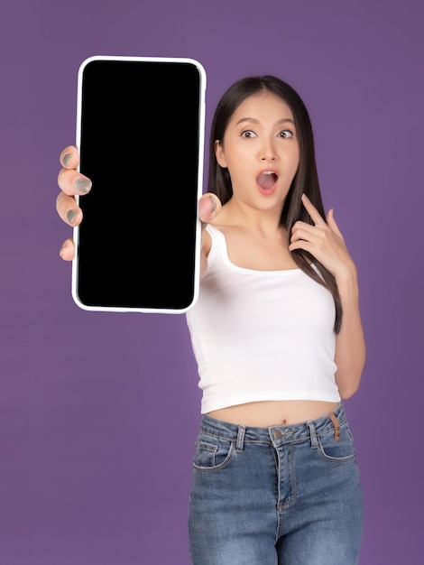 Schöne asiatische junge Frau Aufgeregtes überraschtes Mädchen, das großes Smartphone mit weißem Bildschirm des leeren Bildschirms lokalisiert auf purpurrotem Hintergrund zeigt Mock-up-Bild anzeigen