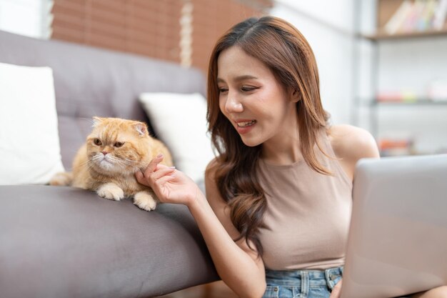 Schöne asiatische junge Frau benutzt Laptop, während ihre Katze zu Hause auf dem Sofa im Wohnzimmer sitzt