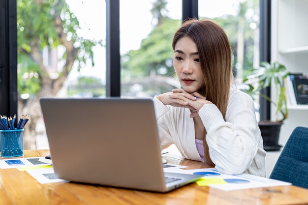 Schöne asiatische junge Frau, die Informationen über einen Laptop, Konzeptbild der asiatischen Geschäftsfrau betrachtet, die intelligente, moderne weibliche Führungskraft, Startgeschäftsfrau, Geschäftsführerfrau arbeitet.