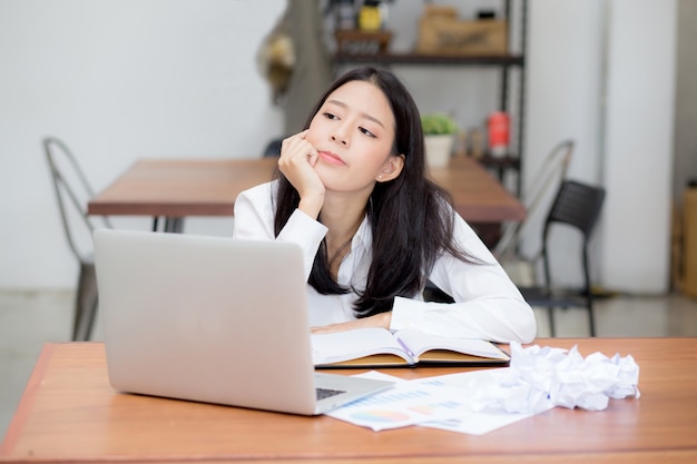 Schöne asiatische junge Frau, die on-line-Problem mit Laptop bearbeitet.