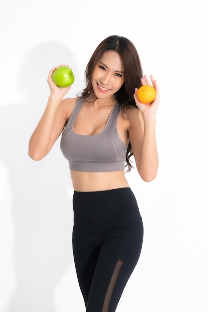 Foto schöne asiatische junge frau gesundes essen in trainingskleidung mit grünem apfel und orange mit gesundem essen isoliert auf weißem hintergrund