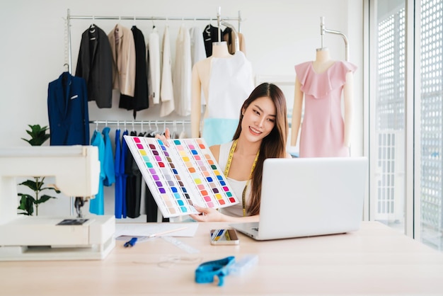 Schöne asiatische Modedesignerinnen oder Schneiderinnen zeigen dem Kunden im Online-Meeting die Musterstoffmuster. Modedesignerin arbeitet im Studio, Kleinunternehmenskonzept