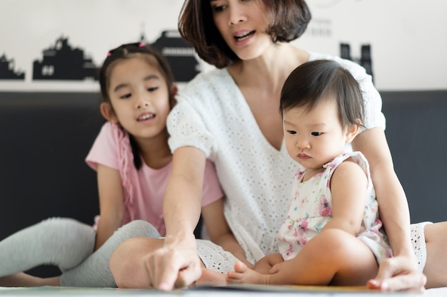 Schöne asiatische Mutter, die ziemlich Geschichtengeschichtenbuch mit ihren Kindern auf dem Bett liest.