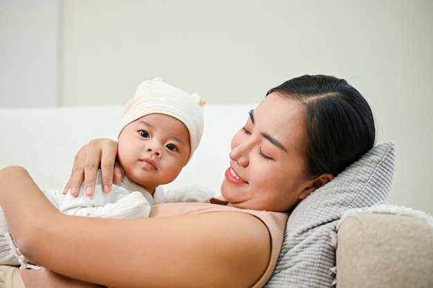 Schöne asiatische Mutter hält ihren kleinen Jungen, während sie sich auf dem Sofa entspannt