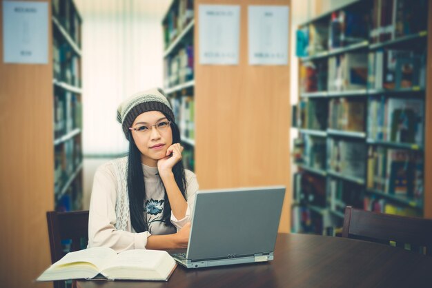 Schöne asiatische Studentin, die einen Laptop für das Studium in der Bibliothek benutzt, liest sie vor dem offenen Laptop