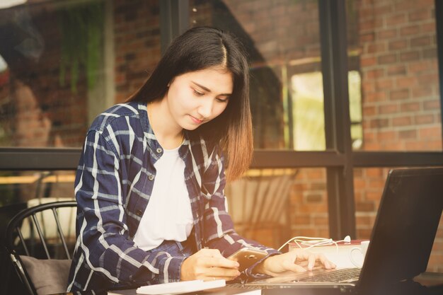 schöne Asien-Frau, die den Computer und Handy arbeitet mit glücklichem verwendet