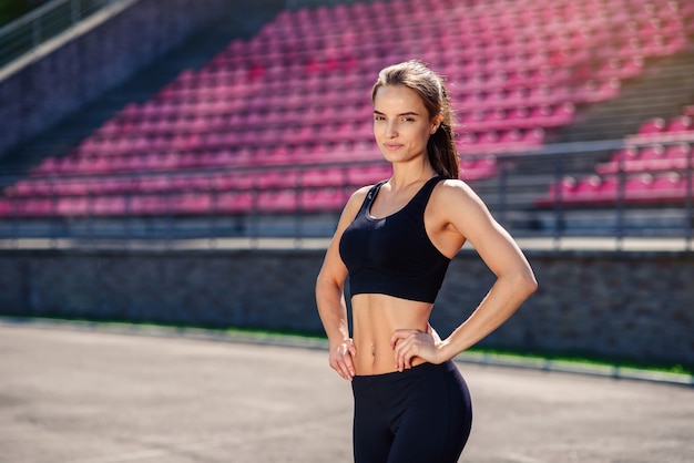 Schöne athletische Frau mit fitem Körper in schwarzer Sportbekleidung ruht nach dem Training